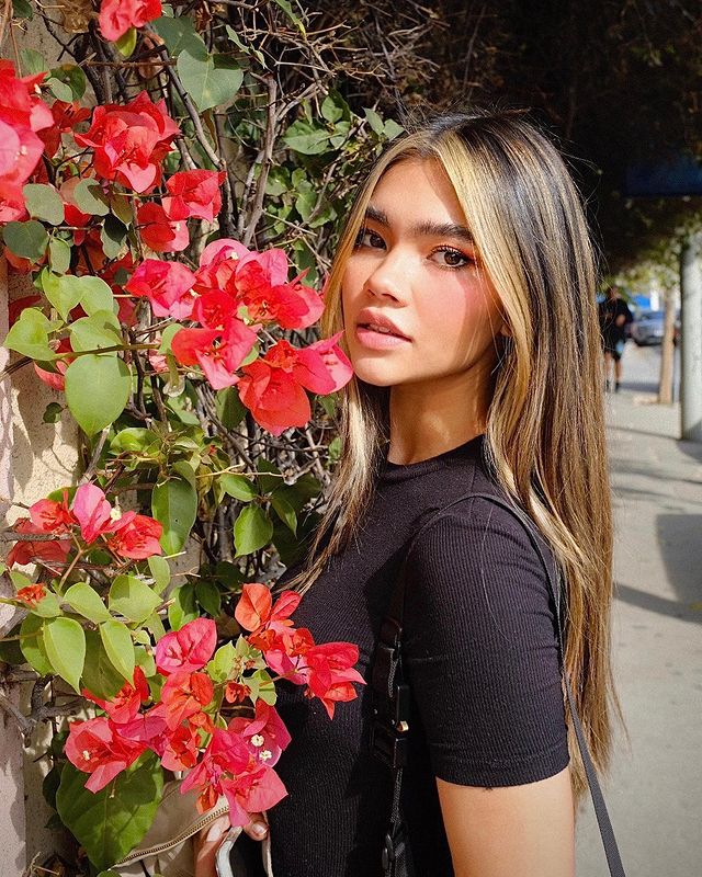 Myra Molloy in a black t-shirt posing in front of red flowers.